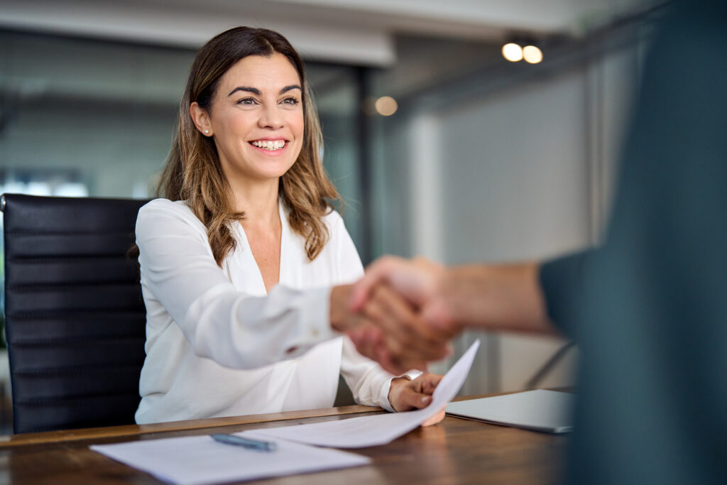 A woman in a professional setting shaking hands with hiring manager representing the opportunities candidates can access by joining AccountMakers