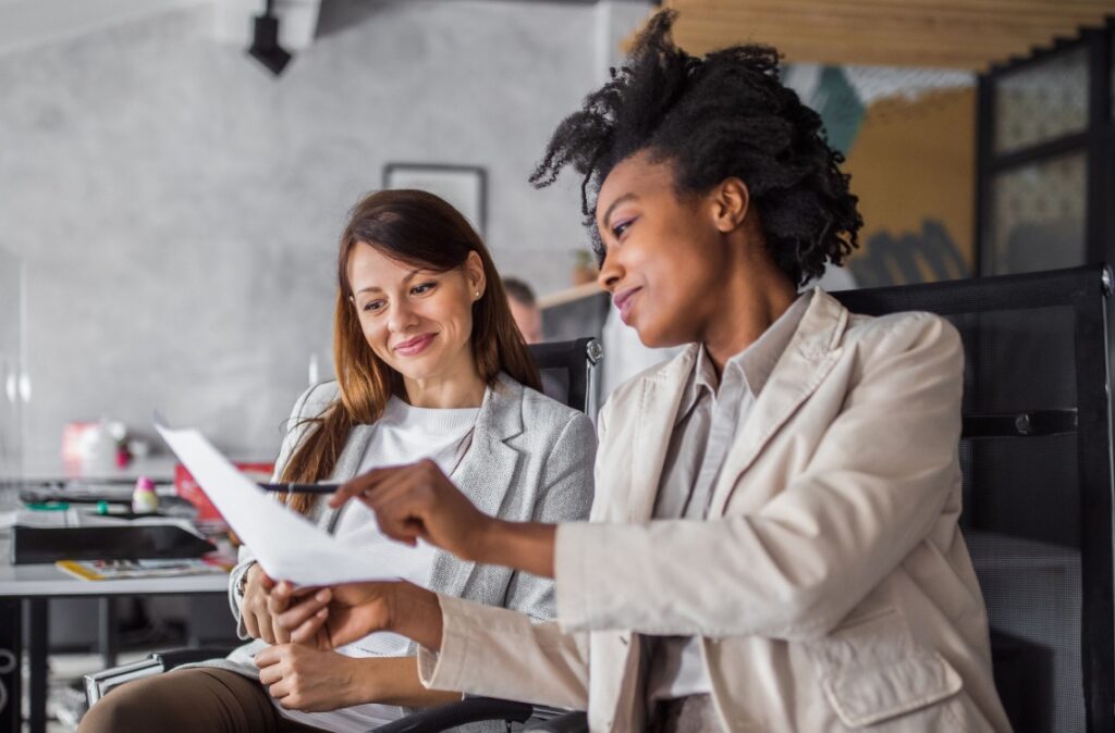 “New sales team members sitting in their office chairs and reviewing reports together at work, after being placed by AccountMakers.