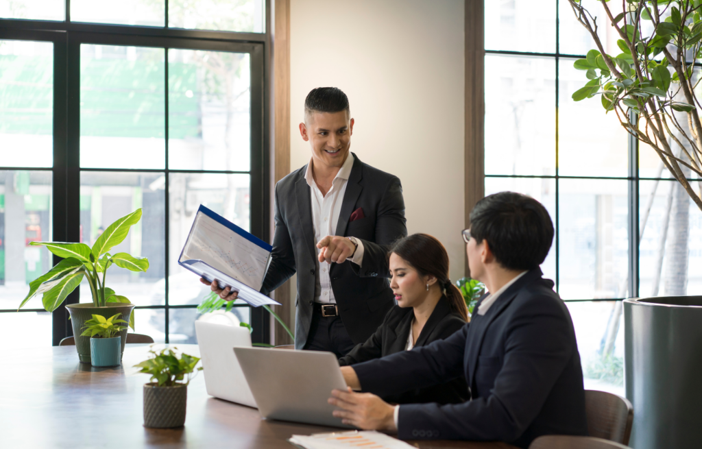 Orange County Sales Hiring - image of Orange County sales team sitting at office table looking at computers and binder with sales information