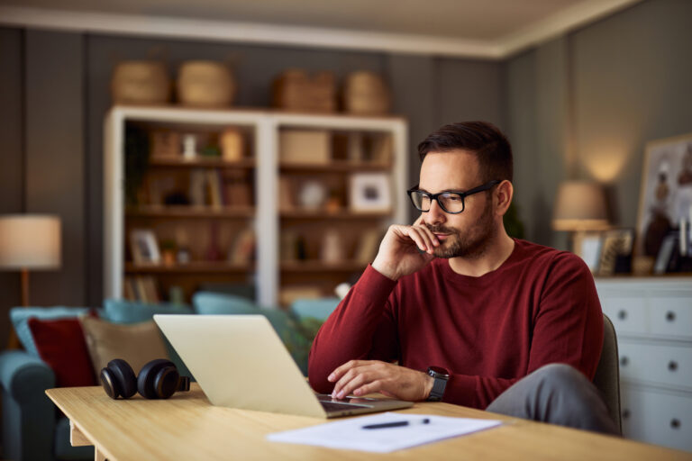 Remote sales jobs worker at home at his laptop thinking with hand on his chin looking serious.
