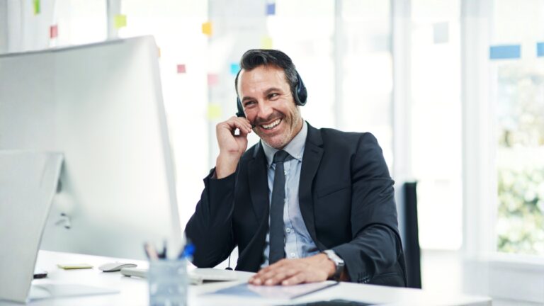 Professional man in black suit on the phone at his desk in front of his computer.
