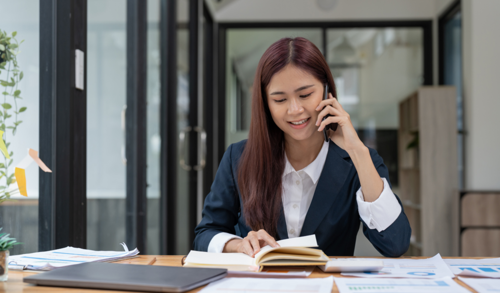 Temp Sales Staffing - image of saleswoman talking on phone looking at notebook at desk in office