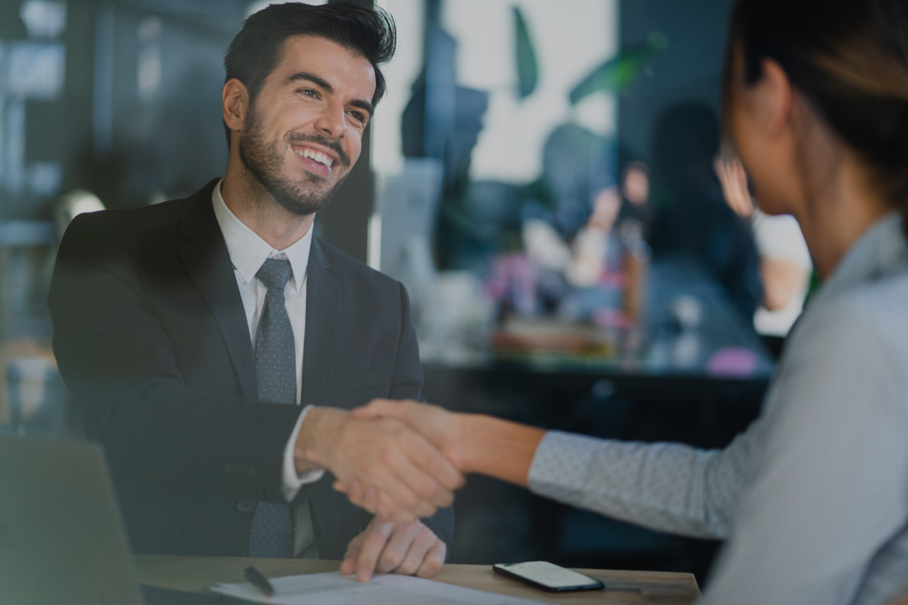 Temporary Customer Success Staffing - image of customer success professional shaking hands with client at desk with cellphone in view and smiling