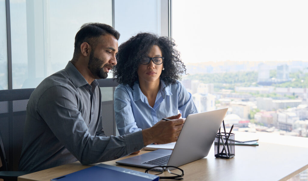 Immediate Temporary sales staffing services image of temporary sales employees sitting in an office reviewing a sales report on a laptop focused and collaborating