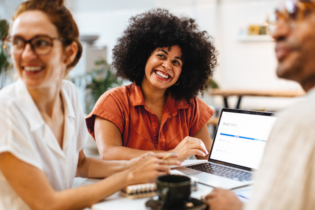 Three professionals collaborating around a laptop in an office, representing how AccountMakers helps companies address customer service and support hiring challenges by connecting them with qualified talent to handle inquiries, resolve issues, and deliver positive customer experiences.